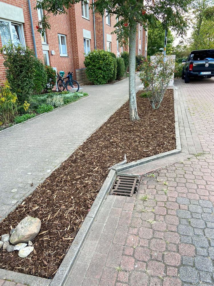 Frisch gemulchtes Beet entlang eines gepflasterten Weges in einer Wohnanlage